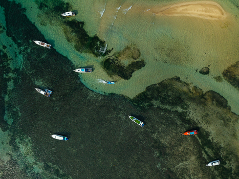 Aerial view of several small boats navigating the shallow turquoise waters and coral reefs near a sandy beach in Kecamatan Denpasar Selatan Bali Indonesia.