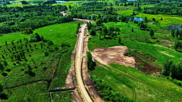 Aerial view of a dirt maintenance road winding through a lush green rural landscape with scattered trees fields and small ponds in Latvia. Aerial view of a dirt maintenance road winding through a lush green rural landscape with scattered trees fields and small ponds in Latvia.