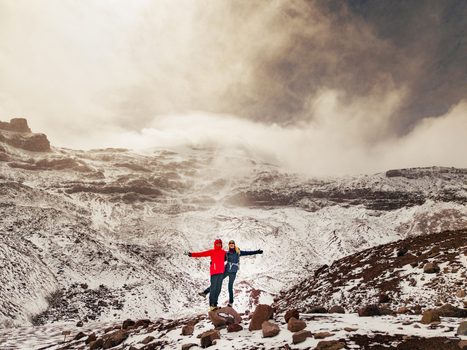 Aerial view of two people standing with arms outstretched on the snowy slopes of Volcano Chimborazo with rugged mountain terrain in Guano Chimborazo Ecuador. Aerial view of two people standing with arms outstretched on the snowy slopes of Volcano Chimborazo with rugged mountain terrain in Guano Chimborazo Ecuador.