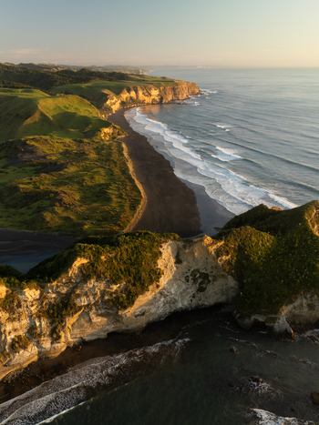 Aerial view of dramatic cliffs meeting the dark sand beach where waves crash golden light kissing the landscape Waikawau Waikato Region New Zealand. Aerial view of dramatic cliffs meeting the dark sand beach where waves crash golden light kissing the landscape Waikawau Waikato Region New Zealand.