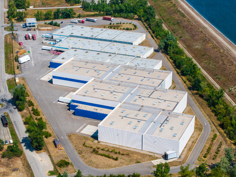 Aerial view of Hombourg Logistic park featuring large industrial warehouses with flat roofs loading docks and surrounding paved areas near a canal in Hombourg Grand Est France.