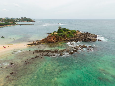Aerial view of Parrot Rock island surrounded by turquoise ocean water and a sandy beach with people at Mirissa Southern Province Sri Lanka. Aerial view of Parrot Rock island surrounded by turquoise ocean water and a sandy beach with people at Mirissa Southern Province Sri Lanka.
