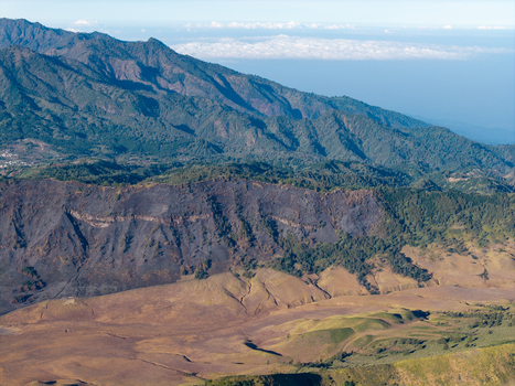 Aerial view of Bromo Tengger Semeru National Park showing wildfire aftermath with scorched earth and green vegetation on rugged mountain slopes in Tosari East Java Indonesia.