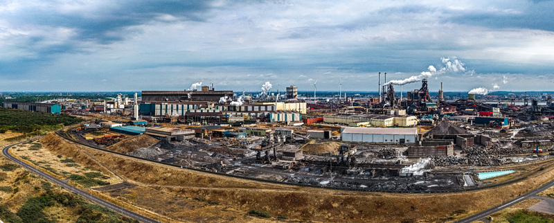 Aerial view of the Tata Steel industrial complex with smoking chimneys large factory buildings and storage yards in Velsen Noord Noord Holland Netherlands. Aerial view of the Tata Steel industrial complex with smoking chimneys large factory buildings and storage yards in Velsen Noord Noord Holland Netherlands.