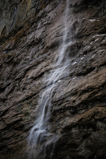 View of delicate waterfalls cascade down the rugged textured face of a steep rock cliff creating a serene and breathtaking scene Lauterbrunnen Switzerland. View of delicate waterfalls cascade down the rugged textured face of a steep rock cliff creating a serene and breathtaking scene Lauterbrunnen Switzerland.