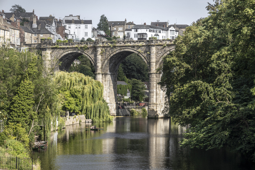 View of Knaresborough Viaduct spanning the River Nidd with historic stone arches lush green trees and traditional houses in Knaresborough England United Kingdom.