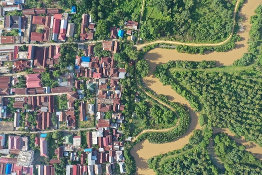 Aerial view of Pulau Maginti featuring a dense residential area with red roofed houses adjacent to a winding river and lush tropical vegetation in Maginti South East Sulawesi Indonesia.
