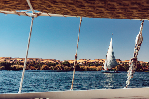View of a traditional felucca sailboat gliding on the Nile River with desert hills and lush riverbanks in the background Aswan Aswan Governorate Egypt. View of a traditional felucca sailboat gliding on the Nile River with desert hills and lush riverbanks in the background Aswan Aswan Governorate Egypt.