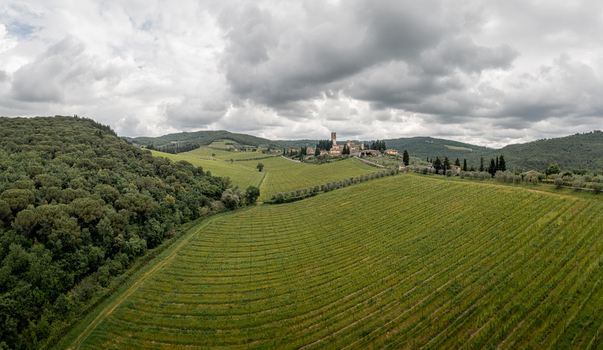 Aerial view of the village of Passignano nestled among rolling hills and lush green vineyards under a cloudy sky in Passignano Toscana Italy. Aerial view of the village of Passignano nestled among rolling hills and lush green vineyards under a cloudy sky in Passignano Toscana Italy.