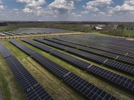 Lebanon United States 12 April 2026 Aerial view of a large solar farm with rows of photovoltaic panels on green grass under a cloudy sky with a red barn in the background.