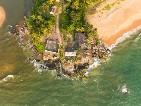 Aerial view of a rocky peninsula with palm trees and a small building next to a sandy beach in Galle Southern Province Sri Lanka.