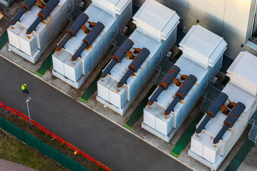 Aerial view of Kao Data industrial power generators and cooling units with a worker in a high visibility jacket walking on the asphalt path in Harlow England United Kingdom. Aerial view of Kao Data industrial power generators and cooling units with a worker in a high visibility jacket walking on the asphalt path in Harlow England United Kingdom.