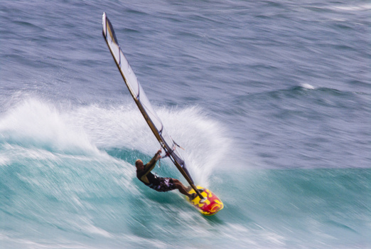 View of a windsurfer riding a powerful turquoise wave with a colorful sail in Kauai County Hawaii United States.