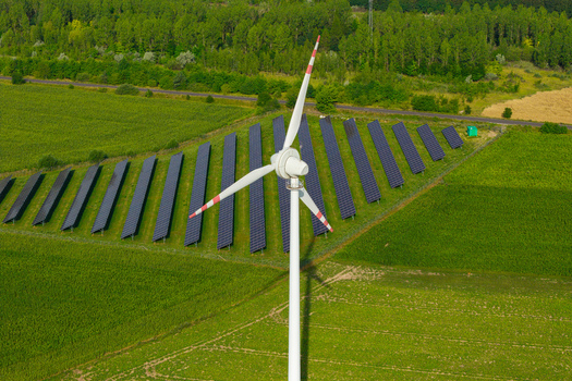 Aerial view of a wind turbine standing in a field of solar panels surrounded by green agricultural land in Poland.