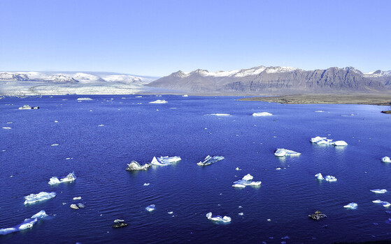 Aerial view of Jokulsarlon Glacier Lagoon with floating icebergs in the deep blue water surrounded by snow capped mountains under a clear sky in Jokulsarlon Iceland. Aerial view of Jokulsarlon Glacier Lagoon with floating icebergs in the deep blue water surrounded by snow capped mountains under a clear sky in Jokulsarlon Iceland.