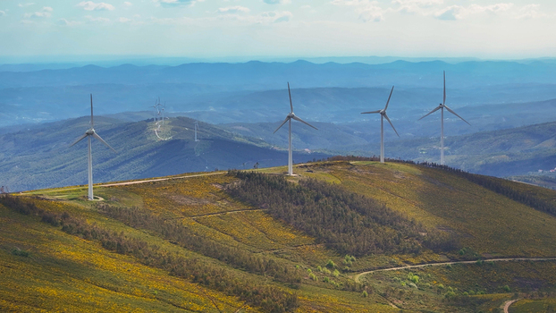 Aerial view of wind turbines situated on a grassy mountain ridge with rolling hills in the background under a clear sky in Lisbon Lisbon Portugal. Aerial view of wind turbines situated on a grassy mountain ridge with rolling hills in the background under a clear sky in Lisbon Lisbon Portugal.