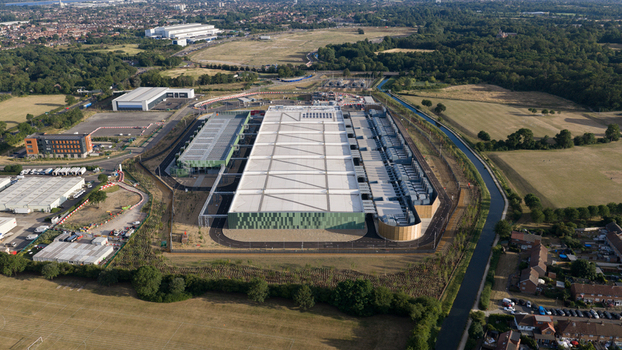 Aerial view of a large modern data center facility with solar panels on the roof surrounded by green fields a canal and suburban housing in Waltham Cross England United Kingdom.