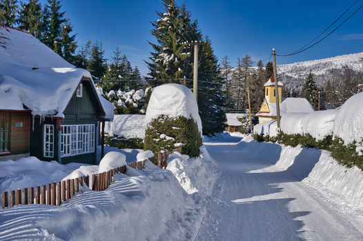 View of a snow laden path winds through a serene village houses adorned with thick blankets of white under a clear blue sky Donovaly Banskobystricky kraj Slovakia. View of a snow laden path winds through a serene village houses adorned with thick blankets of white under a clear blue sky Donovaly Banskobystricky kraj Slovakia.