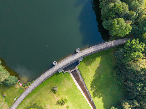Aerial view of the stone dam wall at Fojtka Reservoir surrounded by lush green grass and dense forest in Mnisek Liberecky kraj Czechia. Aerial view of the stone dam wall at Fojtka Reservoir surrounded by lush green grass and dense forest in Mnisek Liberecky kraj Czechia.