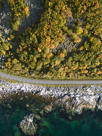 Aerial view of the coastal road near Vik Strand with autumn colored trees and rocky shoreline by the turquoise sea in Leknes Nordland Norway. Aerial view of the coastal road near Vik Strand with autumn colored trees and rocky shoreline by the turquoise sea in Leknes Nordland Norway.