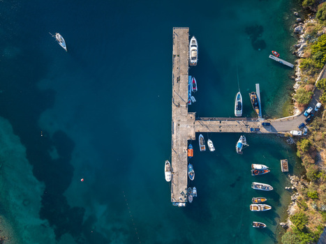 Aerial view of a concrete pier with several boats moored in the turquoise waters of the bay along the rocky coastline Porto Palermo Qarku i Vlores Albania. Aerial view of a concrete pier with several boats moored in the turquoise waters of the bay along the rocky coastline Porto Palermo Qarku i Vlores Albania.