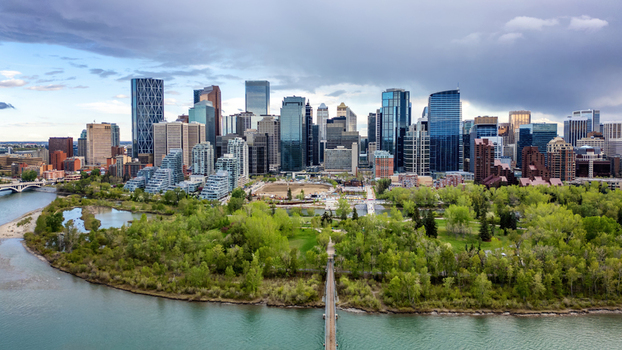 Aerial view of the Calgary skyline rising above the Bow River and lush green trees of Prince s Island Park under a dramatic cloudy sky in Calgary Alberta Canada.