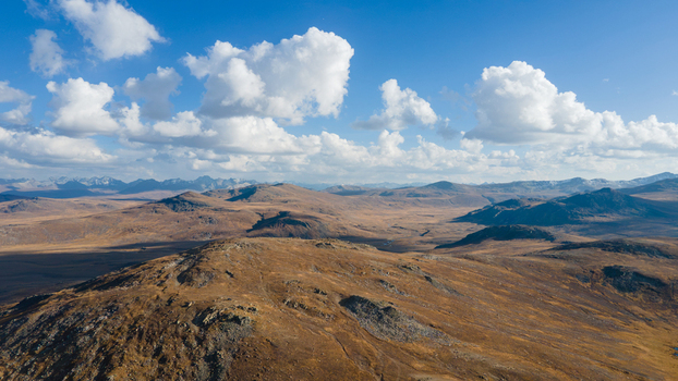 Aerial view of Deosai National Park featuring vast rolling hills rocky terrain and scattered clouds under a clear blue sky in Skardu Gilgit Pakistan.