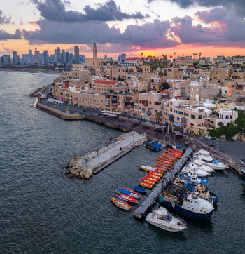 Aerial view of the historic Old port of Jaffa with colorful fishing boats docked at the pier stone buildings and the modern Tel Aviv skyline at sunset in Tel Aviv Yafo Tel Aviv District Israel.