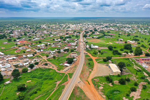 Aerial view of Yapei featuring a main road traversing the town with scattered buildings lush green vegetation and open fields in Yapei Savannah Region Ghana.