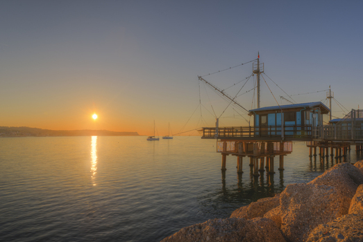View of a traditional fishing structure on the Adriatic coast at sunset with calm water and rocky foreground in Fano Marche Italy. View of a traditional fishing structure on the Adriatic coast at sunset with calm water and rocky foreground in Fano Marche Italy.