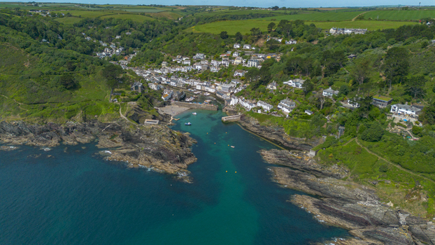 Aerial view of the historic coastal village of Polperro nestled in a rocky cove with turquoise water small boats in the harbor and lush green hills in Polperro Cornwall United Kingdom. Aerial view of the historic coastal village of Polperro nestled in a rocky cove with turquoise water small boats in the harbor and lush green hills in Polperro Cornwall United Kingdom.
