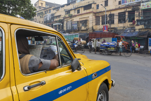 Kolkata India 05 December 2024 View of a yellow taxi cab with a driver reading a newspaper amidst the bustling street life and aged buildings. Kolkata India 05 December 2024 View of a yellow taxi cab with a driver reading a newspaper amidst the bustling street life and aged buildings.