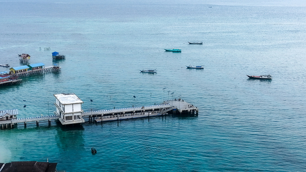 Aerial view of Pulau Derawan with its wooden piers stilt houses over the turquoise sea and small boats floating in the clear water Pulau Derawan East Kalimantan Indonesia. Aerial view of Pulau Derawan with its wooden piers stilt houses over the turquoise sea and small boats floating in the clear water Pulau Derawan East Kalimantan Indonesia.