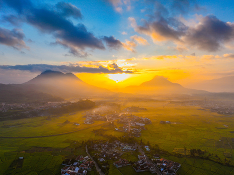 Aerial view of the rural landscape of Kadungora at sunrise with lush green rice fields village houses and mountains shrouded in mist under a golden sky. Kadungora West Java Indonesia. Aerial view of the rural landscape of Kadungora at sunrise with lush green rice fields village houses and mountains shrouded in mist under a golden sky. Kadungora West Java Indonesia.