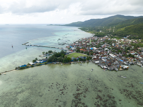 Aerial view of the coastal town where the turquoise sea meets the land with its green vegetation and dense buildings Karimunjawa Central Java Indonesia. Aerial view of the coastal town where the turquoise sea meets the land with its green vegetation and dense buildings Karimunjawa Central Java Indonesia.