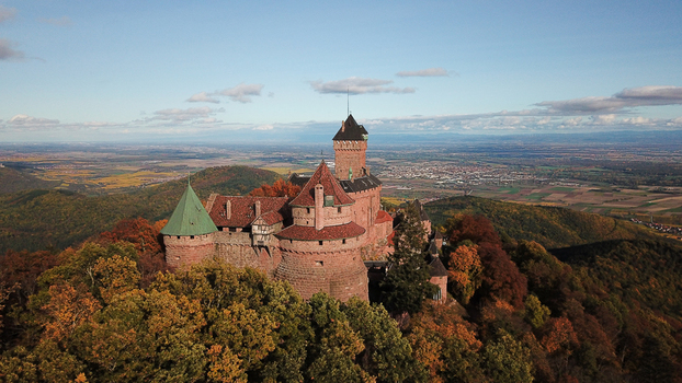 Aerial view of Chateau du Haut Koenigsbourg surrounded by autumn colored forests and rolling hills under a clear blue sky in Orschwiller Grand Est France.