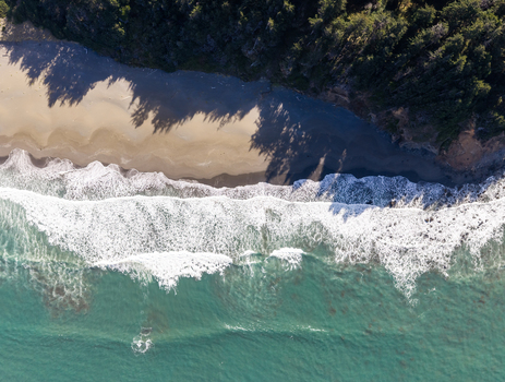 Aerial view of the rugged coastline with turquoise ocean waves crashing onto the sandy beach bordered by dense evergreen forest in Gold Beach Oregon United States. Aerial view of the rugged coastline with turquoise ocean waves crashing onto the sandy beach bordered by dense evergreen forest in Gold Beach Oregon United States.