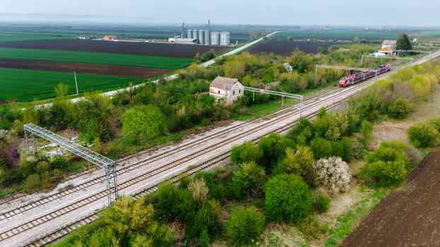 Aerial view of a red train cutting through a vibrant landscape dotted with verdant fields and silver silos Sremska Mitrovica Vojvodina Serbia. Aerial view of a red train cutting through a vibrant landscape dotted with verdant fields and silver silos Sremska Mitrovica Vojvodina Serbia.