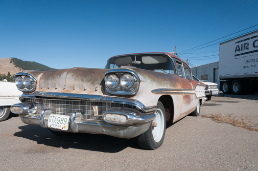 View of a vintage rusty Pontiac classic car parked in an outdoor lot with a semi trailer in the background under a clear blue sky in Langley British Columbia Canada. View of a vintage rusty Pontiac classic car parked in an outdoor lot with a semi trailer in the background under a clear blue sky in Langley British Columbia Canada.