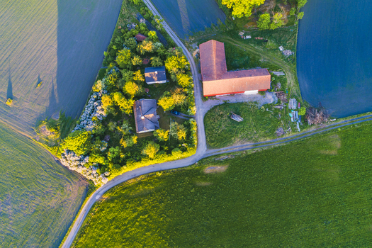 Aerial view of Vanersnas featuring a farmstead with a red barn and residential houses surrounded by lush green fields and trees in Vanersnas Vastra Gotalands lan Sweden. Aerial view of Vanersnas featuring a farmstead with a red barn and residential houses surrounded by lush green fields and trees in Vanersnas Vastra Gotalands lan Sweden.