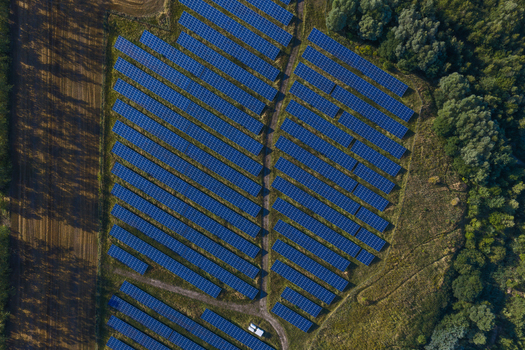 Aerial view of a large solar farm with rows of blue photovoltaic panels arranged in a field surrounded by green trees and agricultural land in Uckermark Brandenburg Germany. Aerial view of a large solar farm with rows of blue photovoltaic panels arranged in a field surrounded by green trees and agricultural land in Uckermark Brandenburg Germany.