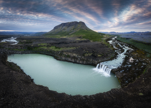 Aerial view of Thjofafoss waterfall cascading into a glacial river surrounded by rugged volcanic terrain and a mountain under a dramatic sky in Rangarthing ytra Iceland. Aerial view of Thjofafoss waterfall cascading into a glacial river surrounded by rugged volcanic terrain and a mountain under a dramatic sky in Rangarthing ytra Iceland.