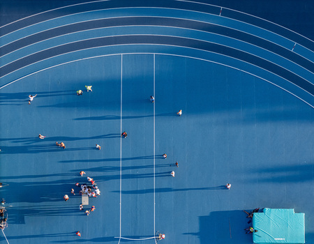Aerial view of a blue running track with athletes training and long shadows cast across the surface in Santo Domingo Distrito Nacional Dominican Republic.