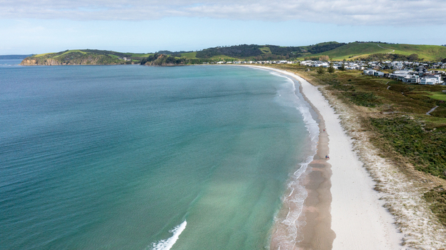 Aerial view of Omaha Beach with turquoise water white sand and coastal houses in Omaha Auckland New Zealand.