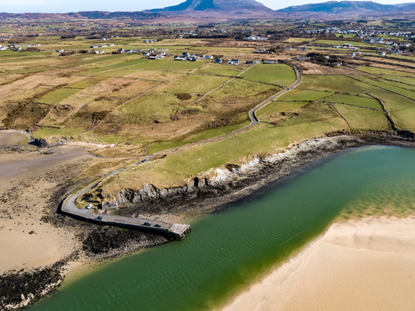 Aerial view of Ballyness Bay featuring a small pier extending into the water surrounded by green agricultural fields stone walls and sandy coastline in Ballyness County Donegal Ireland. Aerial view of Ballyness Bay featuring a small pier extending into the water surrounded by green agricultural fields stone walls and sandy coastline in Ballyness County Donegal Ireland.