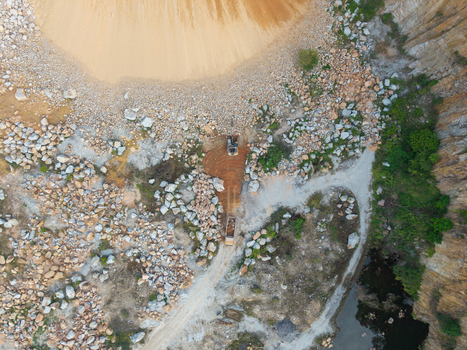 Aerial view of a mining site with an excavator working near piles of rocks dirt paths and a small pool of water in Bukit Tambun Penang Malaysia. Aerial view of a mining site with an excavator working near piles of rocks dirt paths and a small pool of water in Bukit Tambun Penang Malaysia.