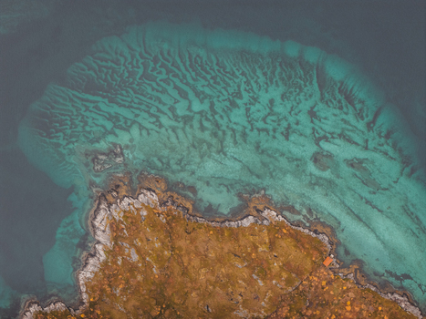 Aerial view of the rugged coastline of Senja with turquoise waters and autumn colored terrain in Senja Troms Norway.