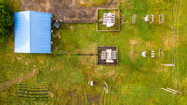 Aerial view of a small electrical substation featuring a blue roofed building transformers and power lines set within a grassy field in Minna Niger State Nigeria. Aerial view of a small electrical substation featuring a blue roofed building transformers and power lines set within a grassy field in Minna Niger State Nigeria.