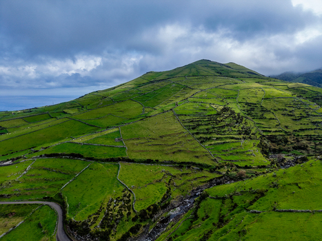 Aerial view of verdant hills cascade down to the sea divided by stone walls under a dramatic sky along Estrada do Farol Flores A&ccedil;ores Portugal.