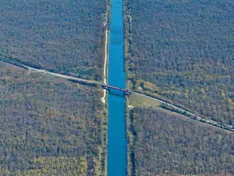 Aerial view of a canal cutting through dense woodland bisected by a bridge the water reflecting the sky above Sausheim Grand Est France.